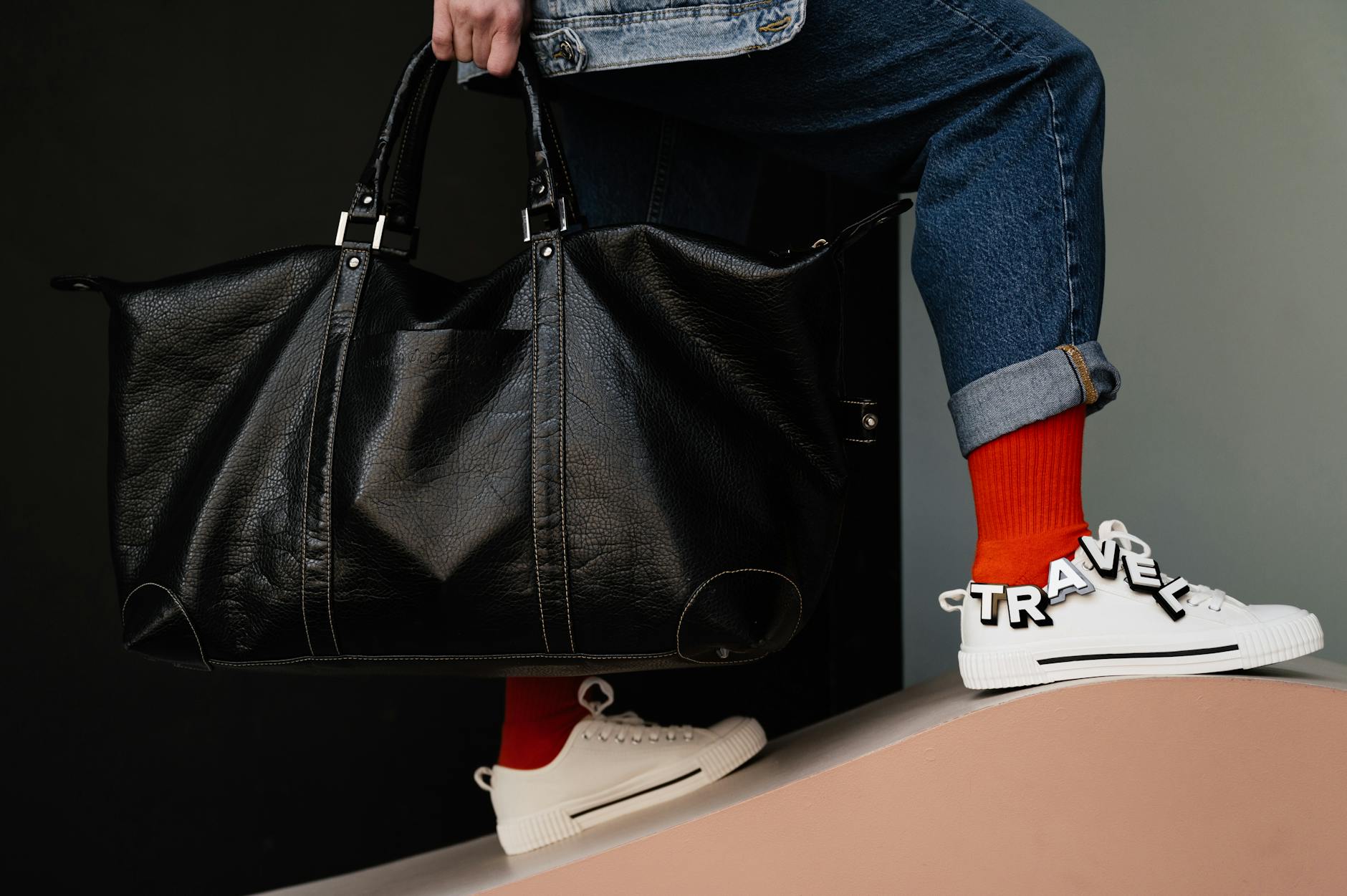 Osoba trzyma skórzaną torbę podróżną i sportowe buty na wyjście Osoba trzyma skórzaną torbę podróżną i sportowe buty na wyjście